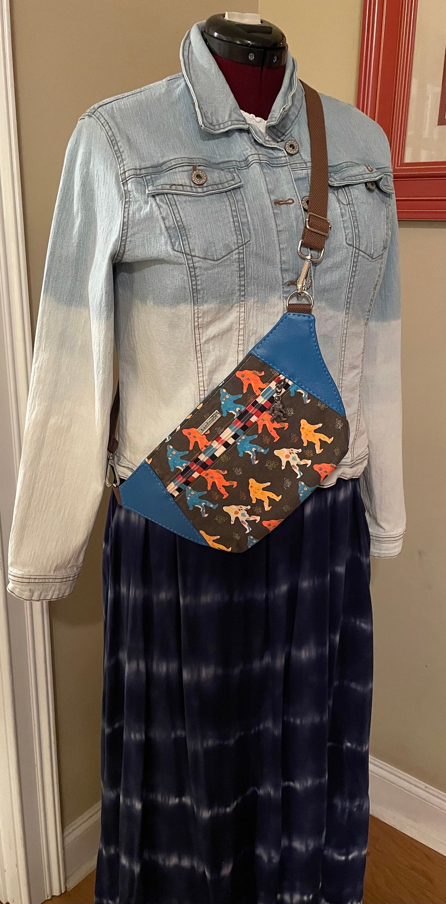 May include: A brown and blue fanny pack with a colorful print of cartoon figures. The fanny pack is worn over a blue denim jacket and a blue and white striped skirt.