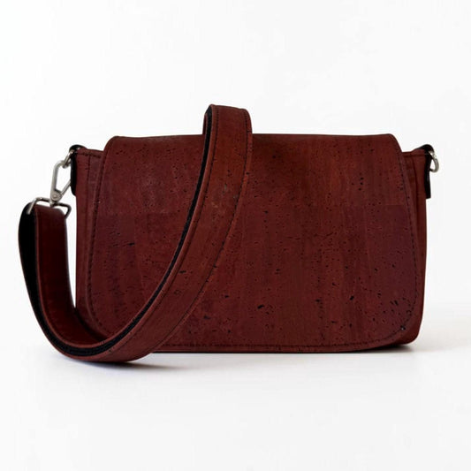 May include: A dark burgundy crossbody bag crafted from textured cork material. The bag features a rectangular flap closure, a wide matching shoulder strap, and silver-toned metal hardware clips on each side to secure the strap to the bag body.